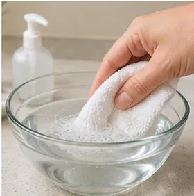 White cleaning cloth being dampened in a small bowl of mild soapy water