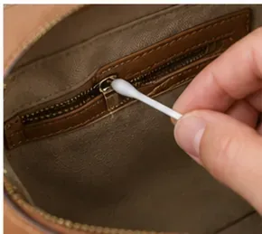 Cotton swab cleaning a narrow seam near the interior zipper of a brown purse