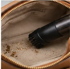 Small vacuum brush removing crumbs and loose debris from the fabric lining inside a brown purse