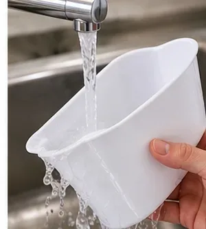 A white pitcher reservoir being rinsed thoroughly under clean running tap water after washing.