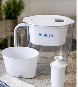 A Brita-style water pitcher disassembled into the clear pitcher, white reservoir, lid, and filter cartridge on a clean kitchen counter.