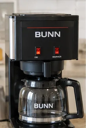 Black BUNN-style home coffee maker with an empty glass carafe positioned beneath the brew funnel