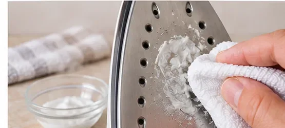 A soft white cloth applying a small amount of cleaning product to a metal iron soleplate
