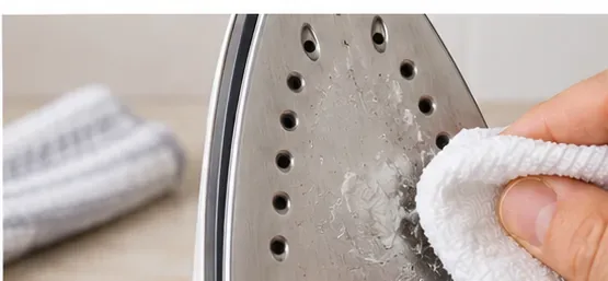 A soft cloth wiping loosened residue from the face of a steam iron soleplate