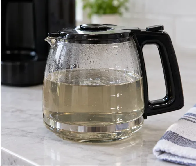 Used descaling liquid collected in a glass carafe after the coffee maker cleaning cycle.