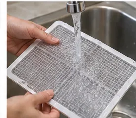 A removable mesh dehumidifier filter being rinsed under a sink faucet.