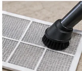 A vacuum cleaner soft brush attachment lifting dust from a removable dehumidifier filter.