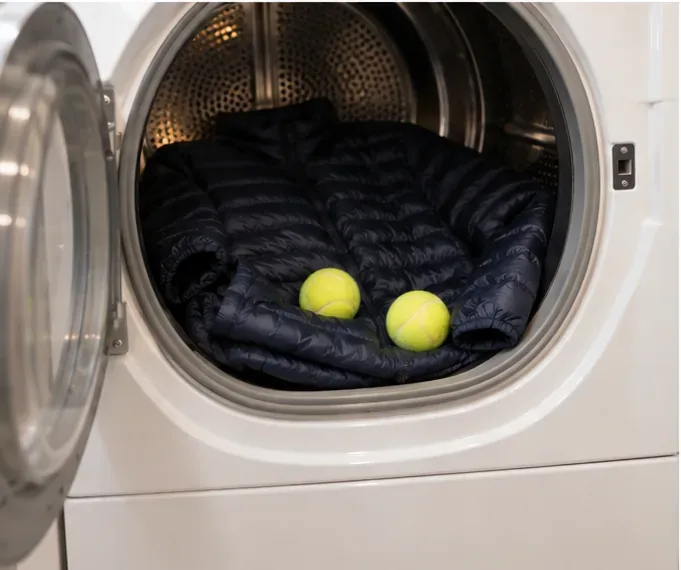 A navy down jacket in a tumble dryer with two clean yellow tennis balls