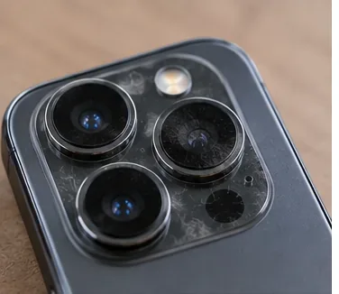 A close-up of a modern phone camera module with visible fingerprints and smudges on the outer camera glass