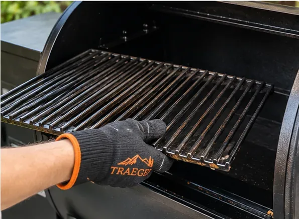 A gloved hand lifting a cooking grate from an open Traeger pellet grill.