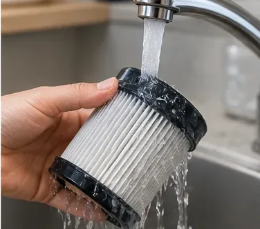 Washable pleated vacuum filter being rinsed under cool running water