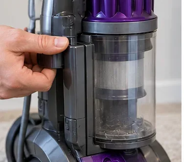 Hand removing the dust bin area of an upright vacuum before taking out the filter