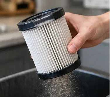 Pleated vacuum filter being gently tapped over a bin to release loose dust