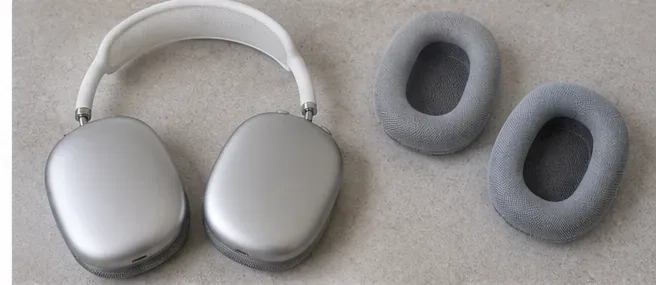 Silver over-ear headphones lying flat on a dry surface with both detached gray cushions placed beside them.