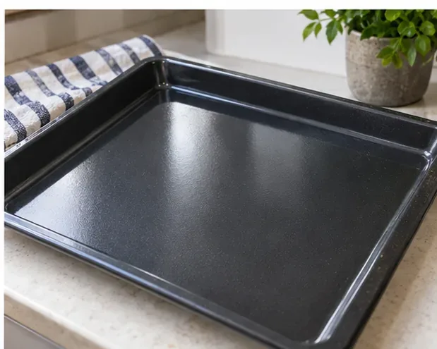 A clean dark oven tray resting on a kitchen counter with an even surface and no visible food residue.