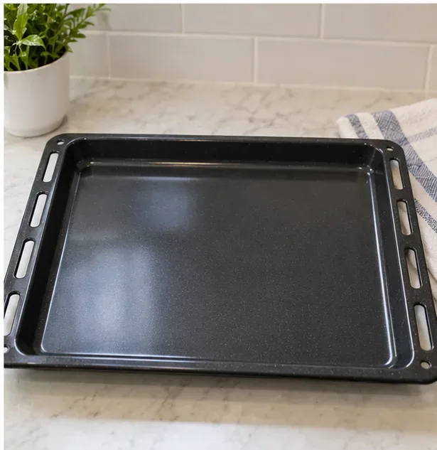 A clean dark oven tray on a bright kitchen counter with a uniform surface and no visible food debris.