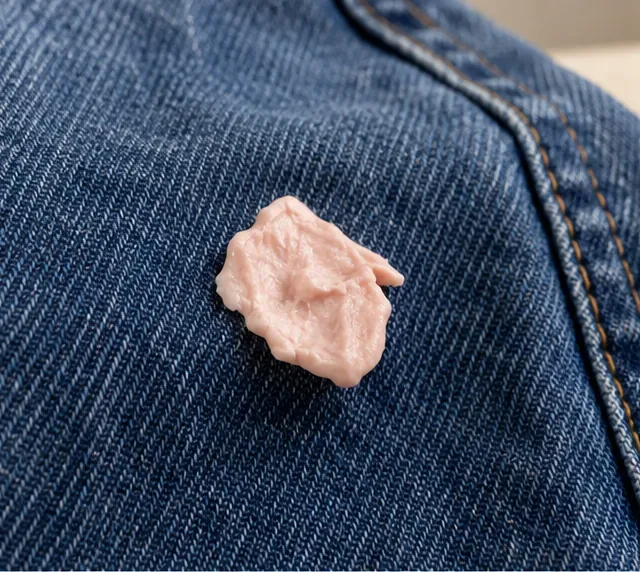 A soft piece of chewing gum stuck to dark blue denim before removal begins.