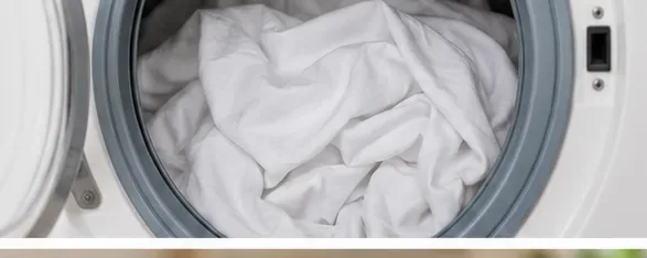 White bed sheets being loaded into a front-loading washing machine