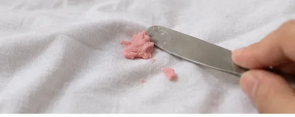 A dull butter knife gently lifting hardened pink gum from a white sheet