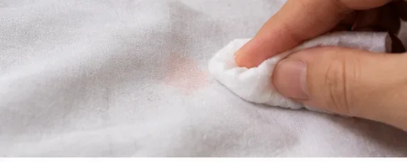 A white cloth dabbing a faint pink residue mark on a white sheet