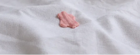 A small piece of pink chewing gum stuck to a white bed sheet