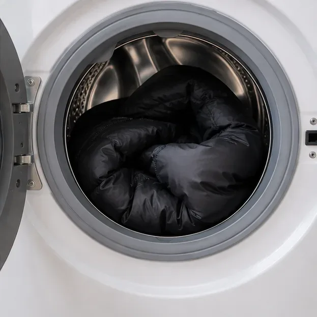 A black puffer sits loosely inside the open drum of a front-loading washing machine.