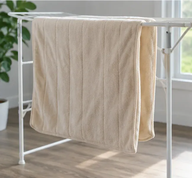 A washed light-colored heated blanket draped loosely over a drying rack to finish air-drying