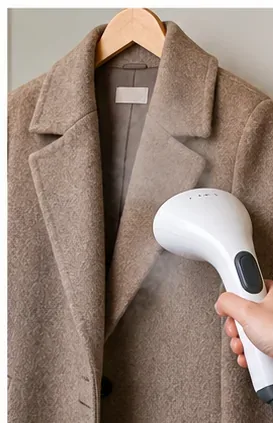 A garment steamer held near the front of a fully dry wool coat hanging on a wooden hanger.