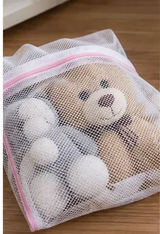 A teddy bear enclosed inside a zippered white mesh laundry bag