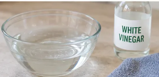 Small glass dish next to a bottle labeled white vinegar and a folded microfiber cloth.