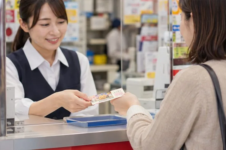 宝くじ売り場の窓口で紙の宝くじ券を店員に差し出す利用者